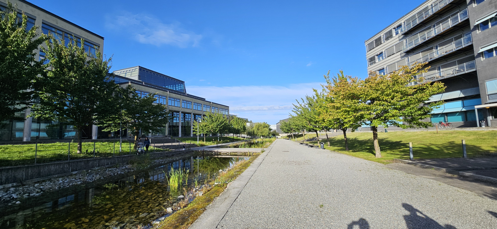A sidewalk in between a row of buildings, and a creek running parallel to the walkway