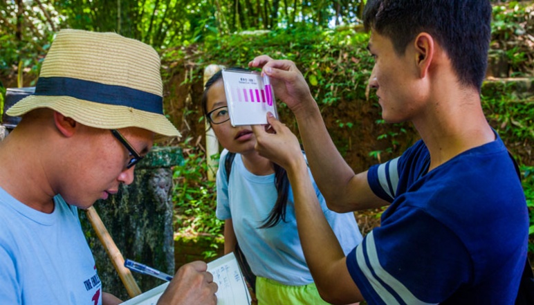Three researchers analyze and take notes on a sample