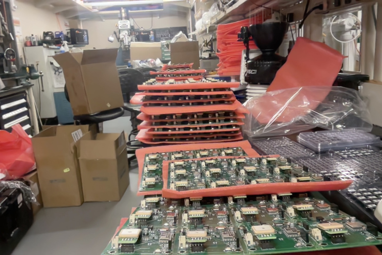 Many circuit boards in a lab with shipping boxes in the background