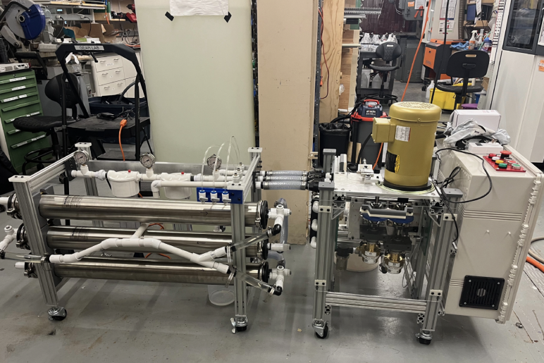 Mechanical device with wires, cylinders, and tubes on metal platforms with wheels in a lab