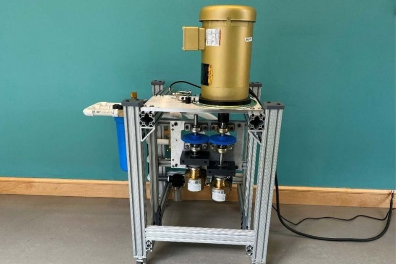 Experimental apparatus with a gold cylinder on top of a metal standing device with levers and tubes