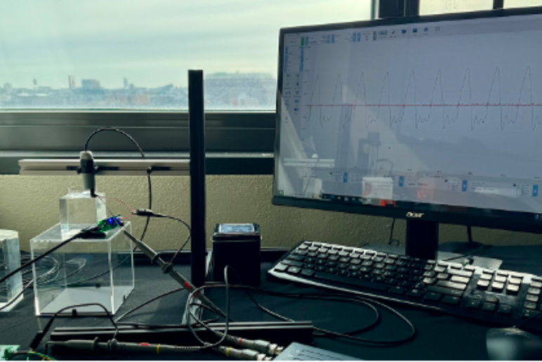 A laboratory setup with experimental equipment connected to a computer displaying a graph, overlooking a cityscape.