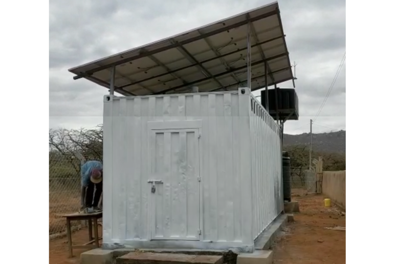White, metal shipping container that has been fitted with a door and solar panels above the container