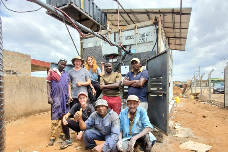 Group of people posing in front of shipping container that has been fitted with solar panels above the container