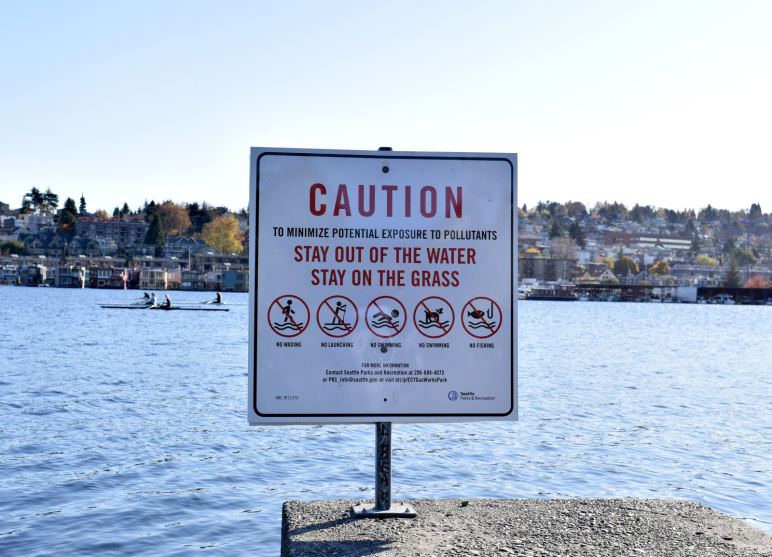 Caution sign that says "To minimize potential exposure to pollutants, stay out of the water stay on the grass"