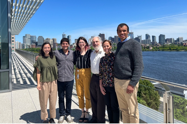 Group of six people standing on a roof deck outside, overlooking the Charles River and Boston