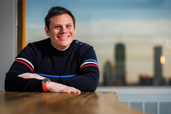 Andrew Babbin sitting at a table in front of a window displaying a city skyline at sunset.