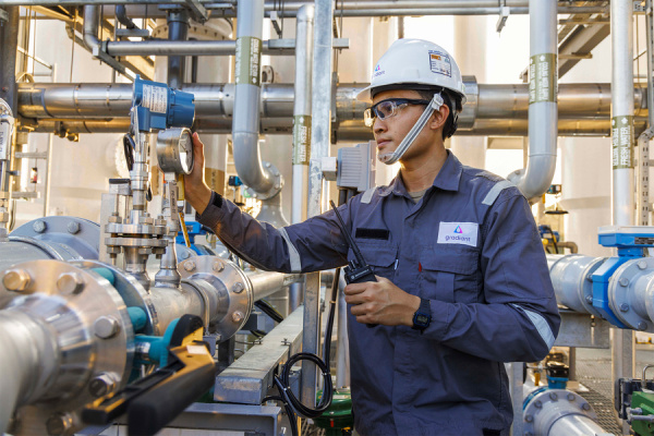 An image of a man in a blue shirt, white hard hat, and work goggles examining a water purification system consisting of piping.