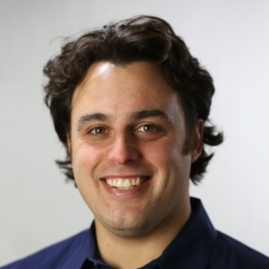 Man with dark hair and purple polo shirt smiles 