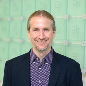 Photograph of Prof. Johnson in a black suit coat and blue purple shirt against a teal green background