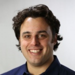 Man with dark hair and purple polo shirt smiles 