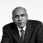 Black and white photo of bald man sitting clasping his hands