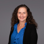 Headshot of Hadley D. Sikes in a blue blouse with a black suit jacket against a gray background