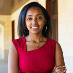 Loza_Tadesse with arms folded wearing red outside a building