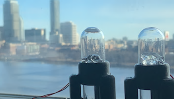 Two sensor devices in front of a window overlooking a city skyline, used for scientific measurements.