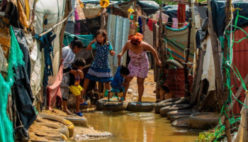 Several people navigating through a flooded alley in a makeshift community using tires as stepping stones.