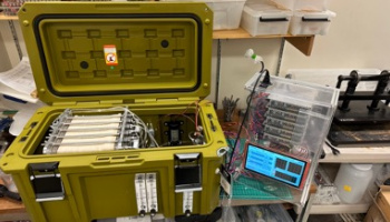 A portable desalination device in a yellow case next to a solar panel sitting on a dock