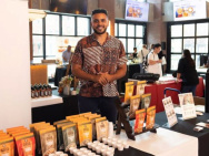 Joshua Reed-Diawuoh stands behind a table with packages of cashew nuts at a trade show