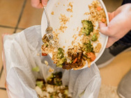 A person’s hands are shown scooping uneaten food off their plate into the trash