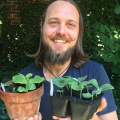 Robbie Wilson smiles and holds three potted plants